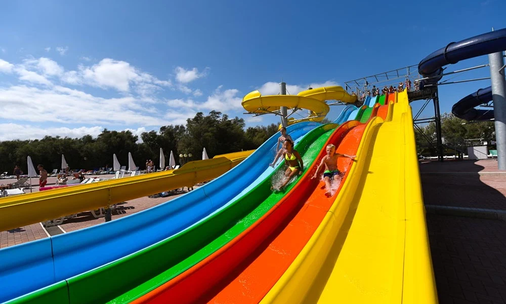 Children sliding down colorful water slides outdoors, with sun loungers and umbrellas in the background at Isamar