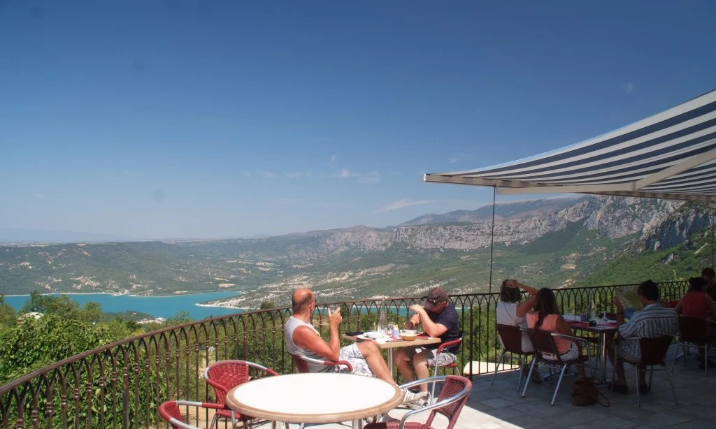 People dining on a terrace with a mountainous landscape and blue lake in the background at de l'Aigle