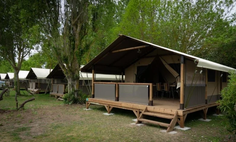 Tented wooden platform lodges stand in a row amidst lush trees, with visible stairs and outdoor seating area at Seasonova Ile de Ré