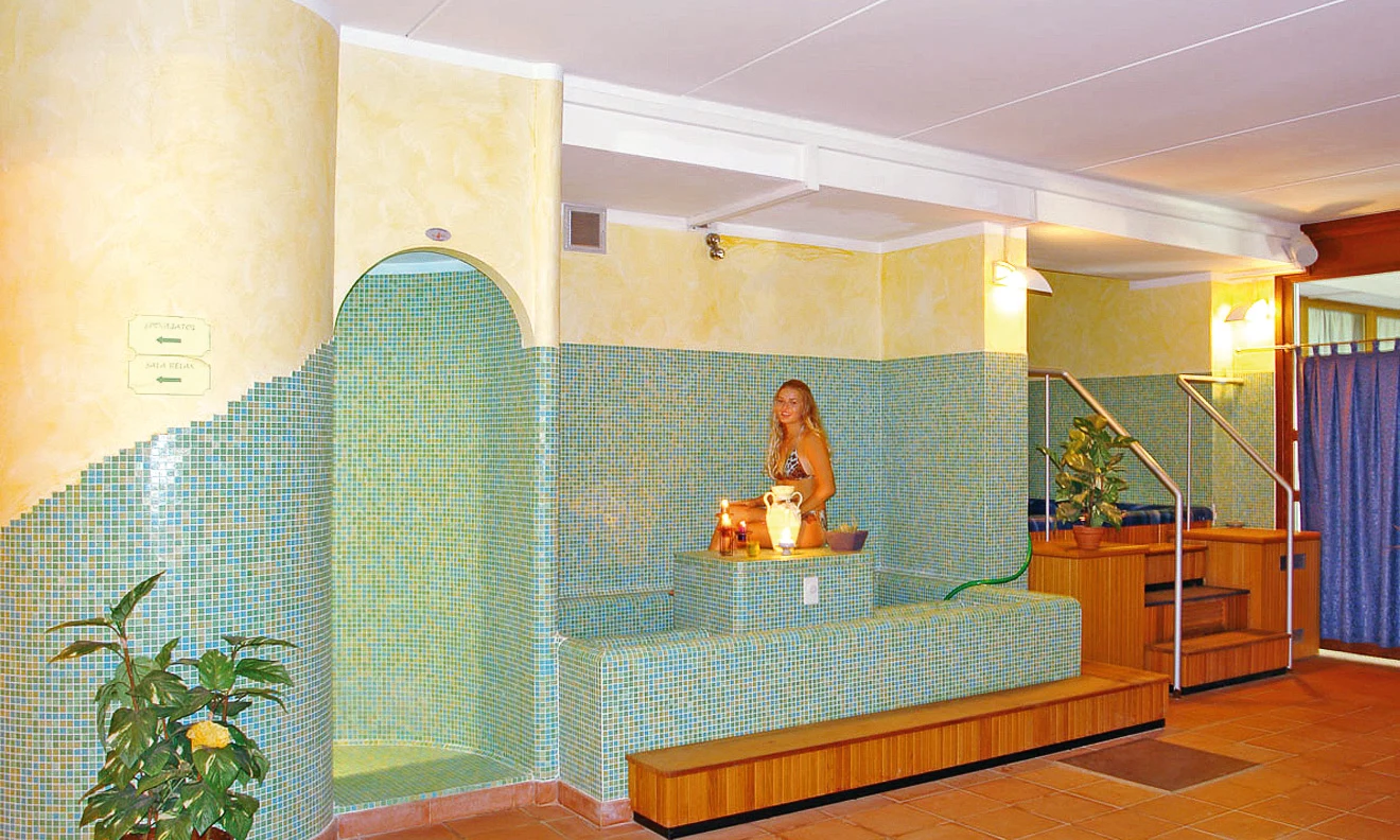 Woman in a bikini standing beside candles and a jug in a tiled spa room at Residence Campi