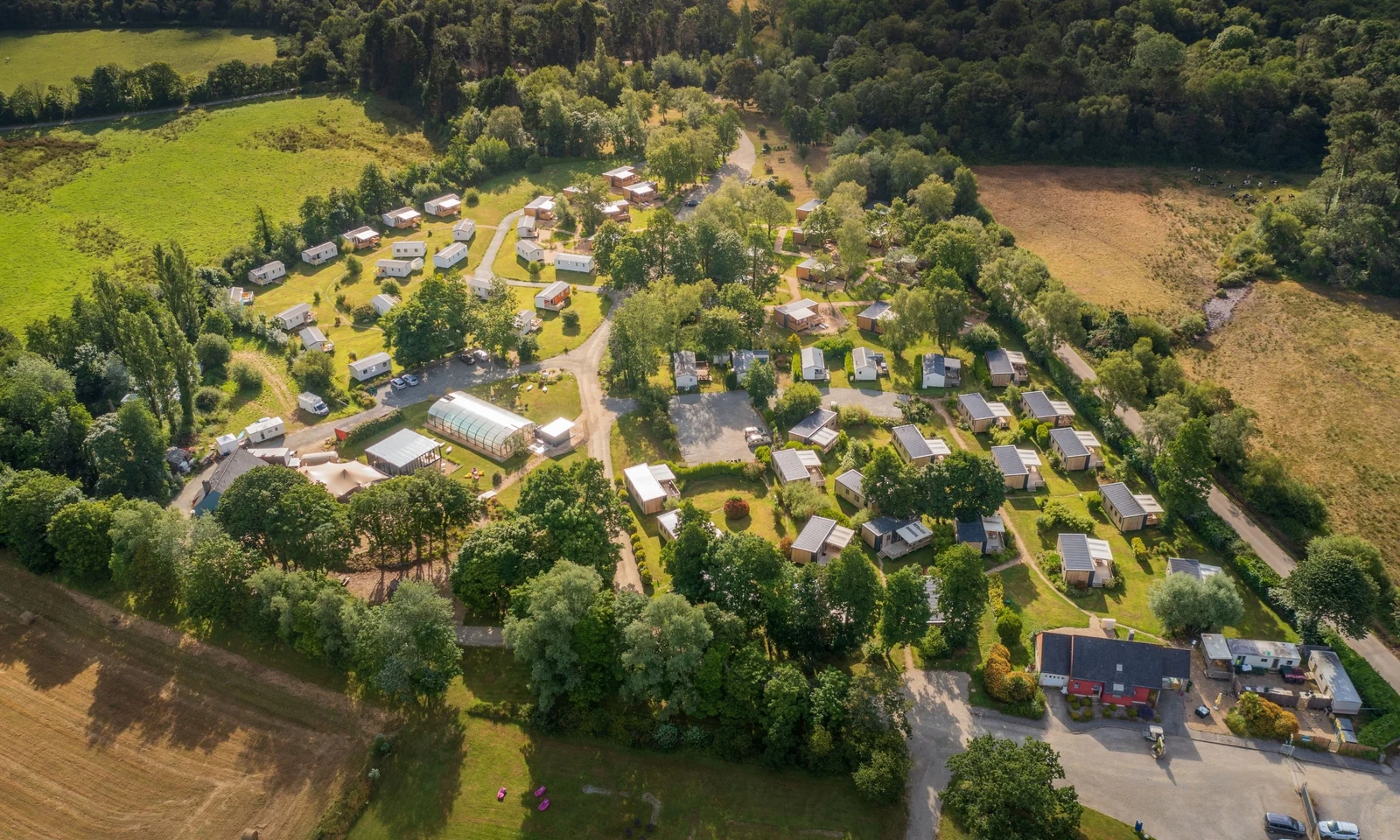 Mobile homes scattered in a lush, green forest setting with open fields surrounding them at Domaine de Mesqueau