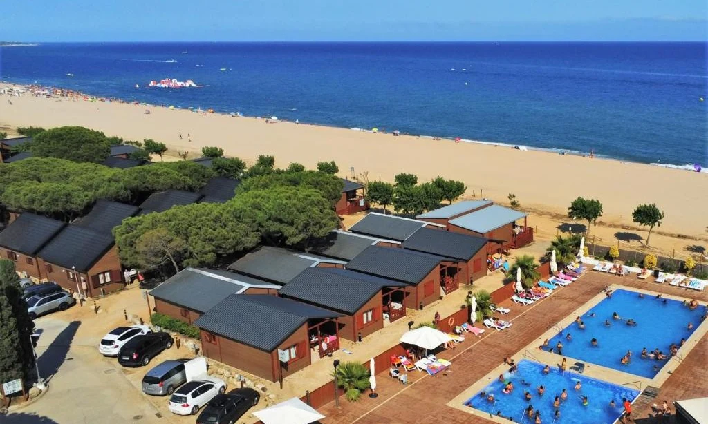 Wooden cabins surrounded by trees, alongside swimming pools and a beach with blue sea at Bon Repos