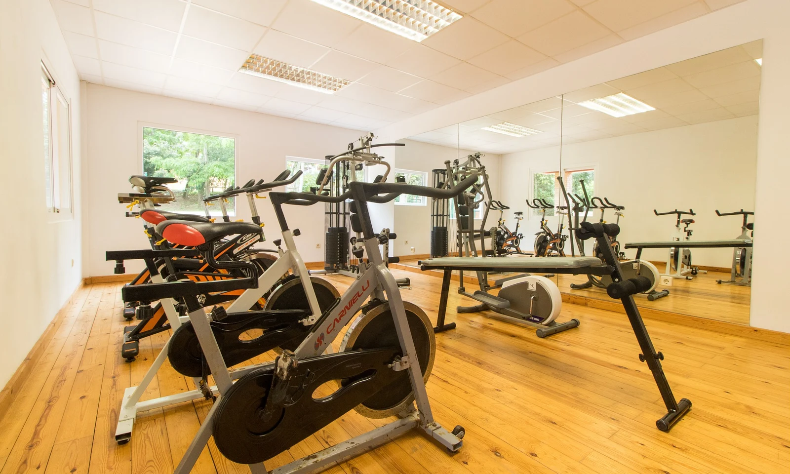 Exercise bikes and fitness equipment, arranged in a bright, spacious gym with wooden floors and large mirrors at Begur