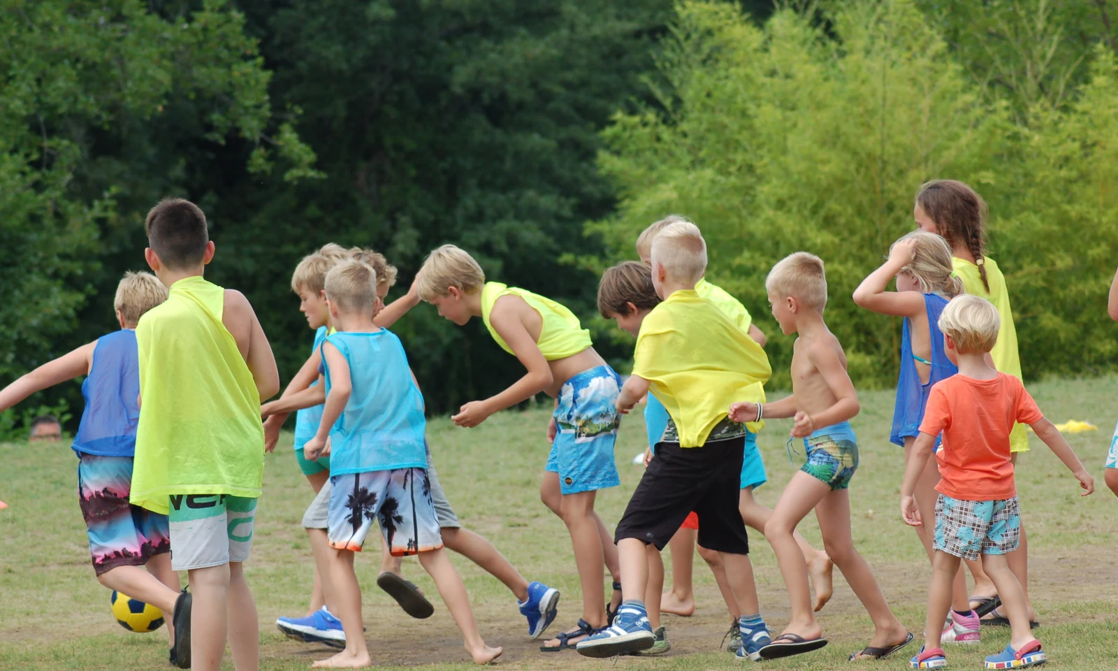 Children playing soccer on a grassy field, wearing colorful jerseys, surrounded by greenery at Les Arches