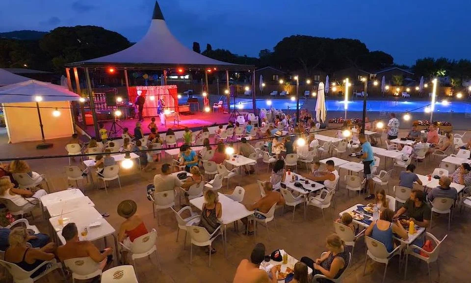 People sitting at tables watching a lit stage beside a lit-up pool at Bon Repos