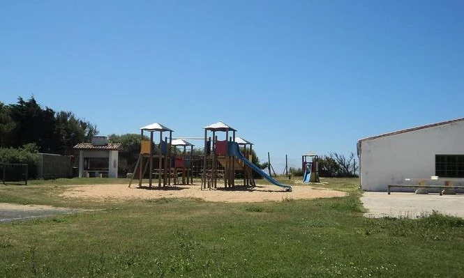 A playground with slides and climbing structures, surrounded by a field and buildings at Seasonova Ile de Ré