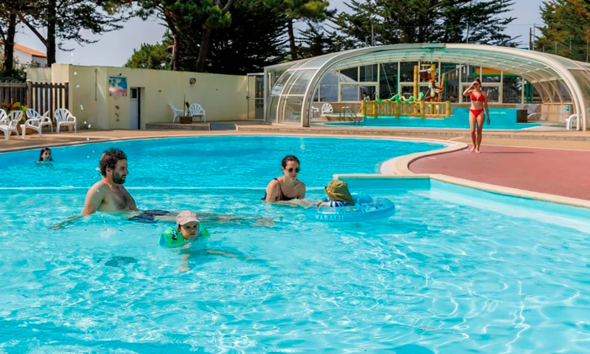 Family swims and relaxes in a pool, with trees and lounge chairs around at Camping 2 Plages & Océan Village Corsaire