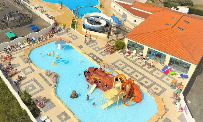 Children playing in a pool with an aquatic playground, surrounded by a deck and a building with a red roof at Les Aventuriers de la Calypso