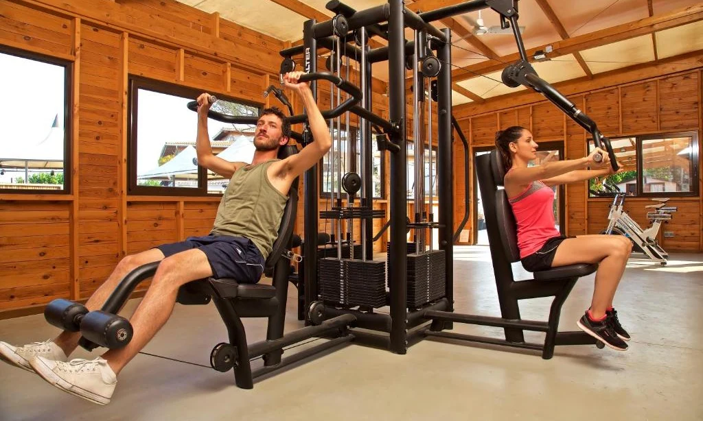 Two individuals exercise on a multi-station gym machine in a spacious, wooden interior at Bon Repos