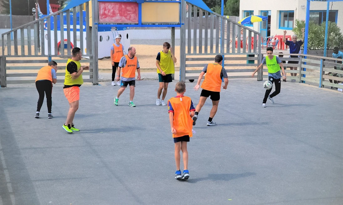 People are playing a game of soccer on a small, enclosed court outside in a recreational area at Les Aventuriers de la Calypso