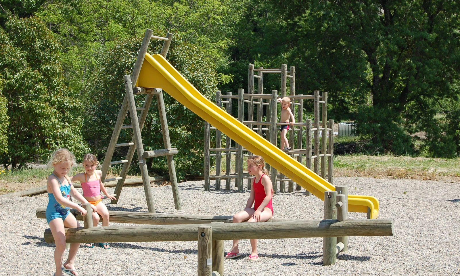 Children playing on playground equipment including a slide and seesaw, surrounded by greenery at Les Arches