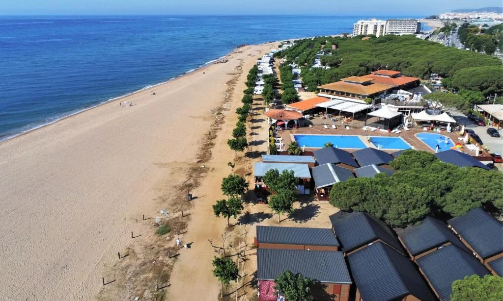 Beachfront campground with cabins and a pool, adjacent to the sandy beach and expansive blue sea under a clear sky at Bon Repos