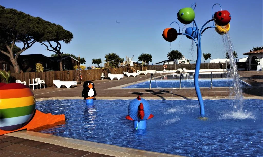 Playfully designed children's pool with colorful slide and water features, surrounded by a paved area with chairs at Bon Repos