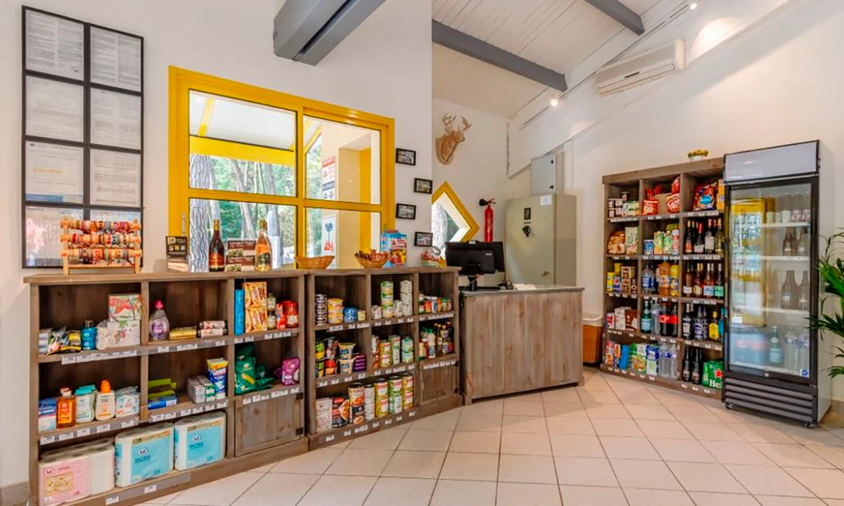 Store shelves displaying various items next to a counter in a brightly-lit room with yellow window frames at Camping 2 Plages & Océan Village Corsaire