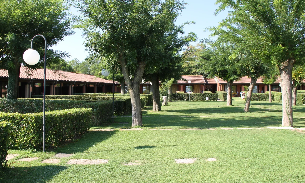 Rows of small, red-roofed buildings lined with trees and bushes, set in a grassy park-like area at Front Lake Resort Le Corti del Lago