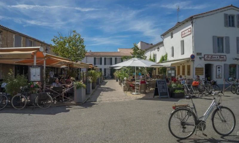 Bicycles parked outside cafes with people dining under umbrellas between buildings at Seasonova Ile de Ré