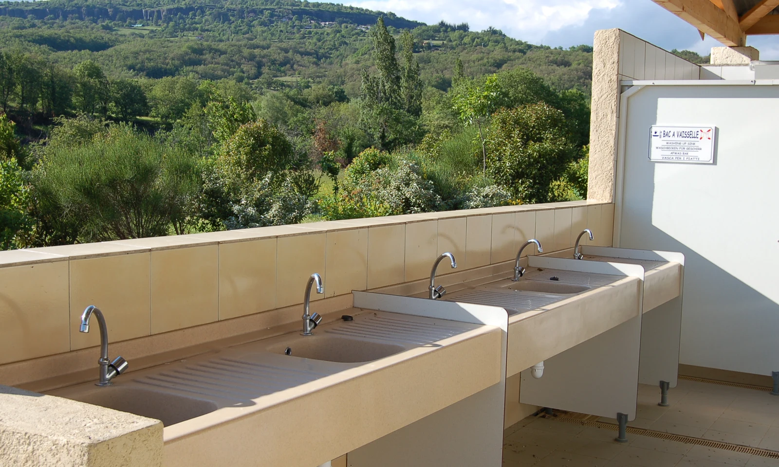 Sinks lined against a tiled wall, under a roof, overlooking a lush, green hillside at Les Arches