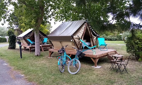 Tents stand on wooden platforms, flanked by trees; two bicycles are parked in front at Seasonova Ile de Ré