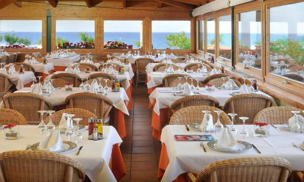 Tables are set with white tablecloths and glassware in a wooden dining room overlooking the sea at Bon Repos