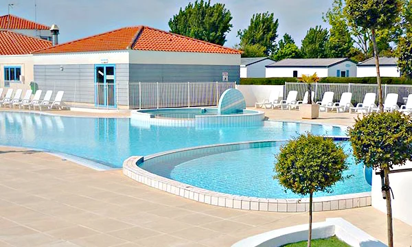 Swimming pool with lounge chairs, bordered by trees and a building with red-tiled roof at Les Aventuriers de la Calypso