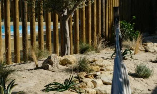 A hammock hangs among rocks and plants beside a wooden fence at Seasonova Ile de Ré