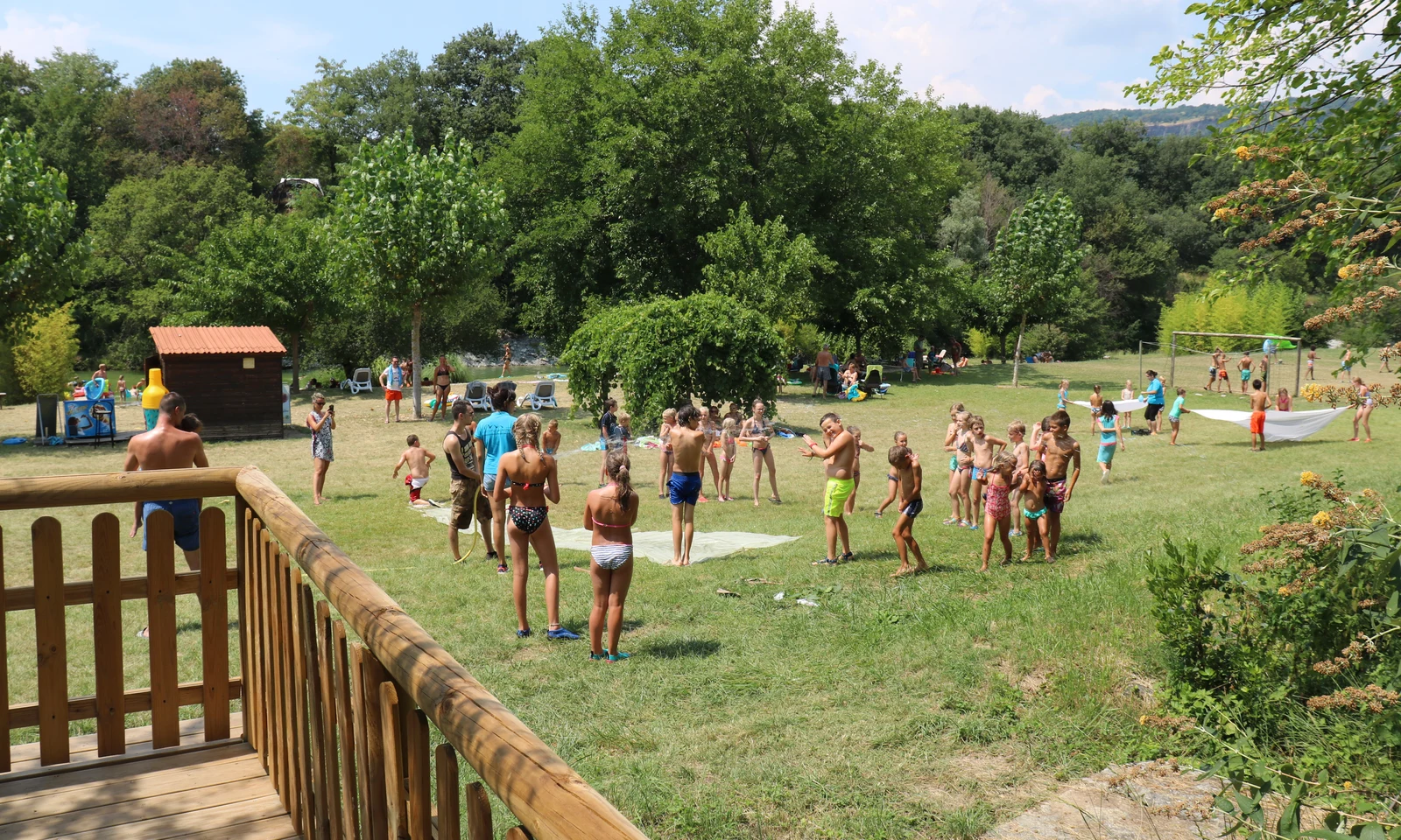 Children engaging in outdoor activities on a grassy field surrounded by trees, adults supervising nearby at Les Arches