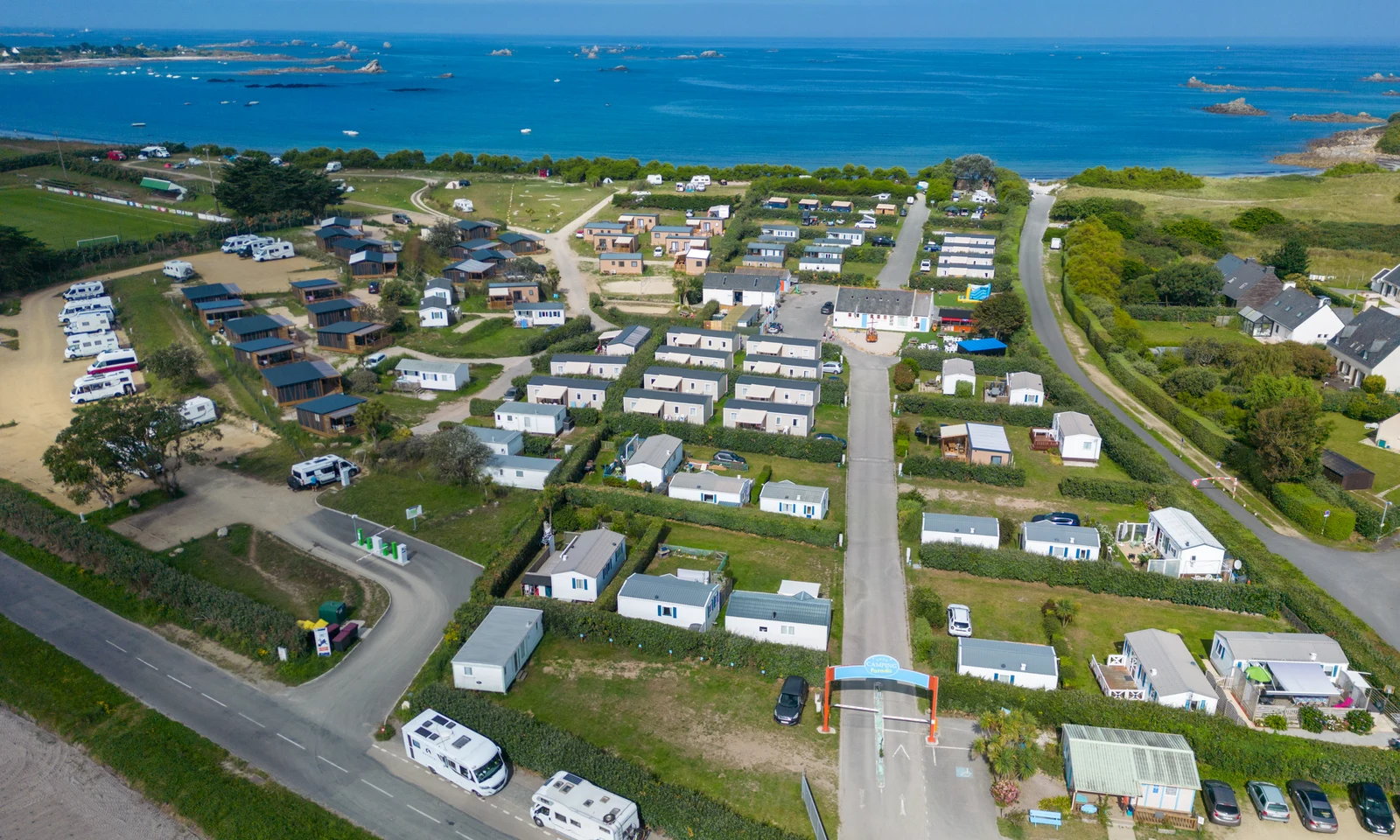 Caravans and mobile homes arranged in rows, situated near a coastal area with clear blue ocean at La Pointe de Roscoff