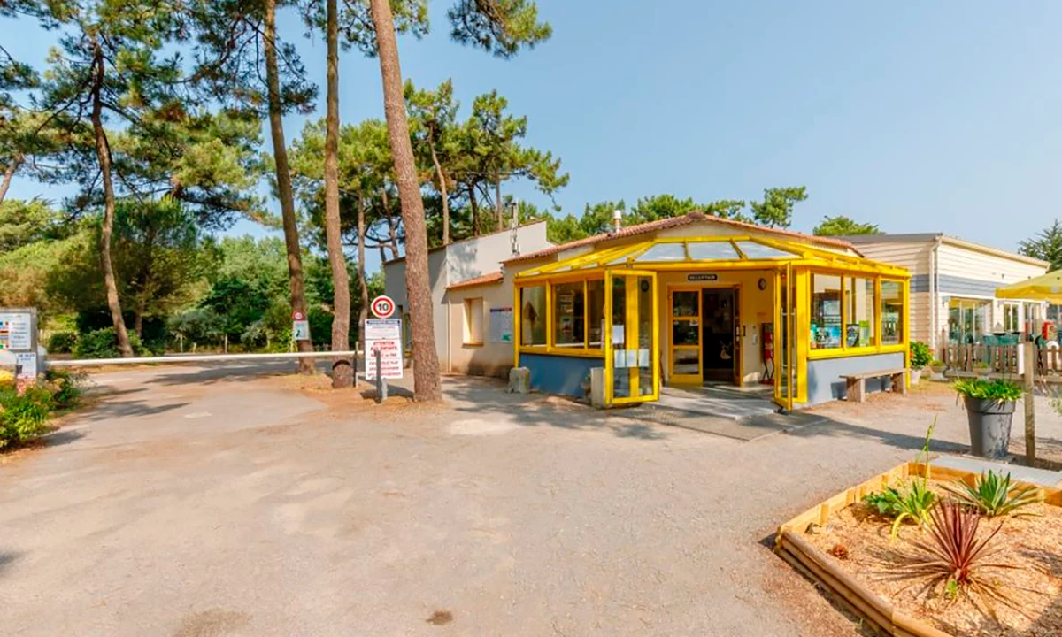 Yellow-fronted building amidst tall trees, serving as a campsite reception area with surrounding greenery at Camping 2 Plages & Océan Village Corsaire