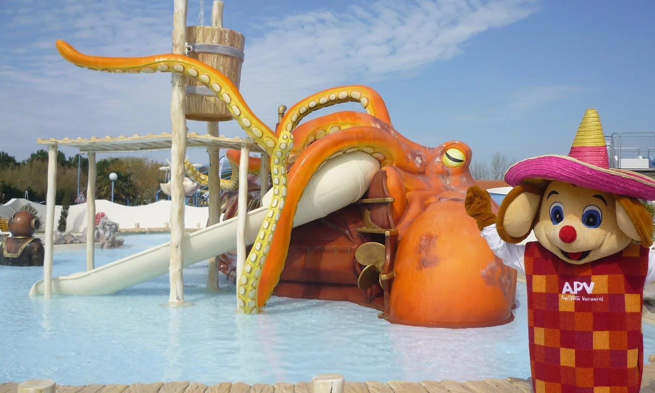 A costumed character waves beside a giant octopus-themed water slide in an outdoor pool area at Les Aventuriers de la Calypso