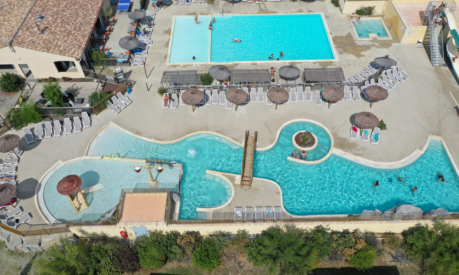 Swimming pools being used by people surrounded by lounge chairs and umbrellas, adjacent to buildings at Les Arches