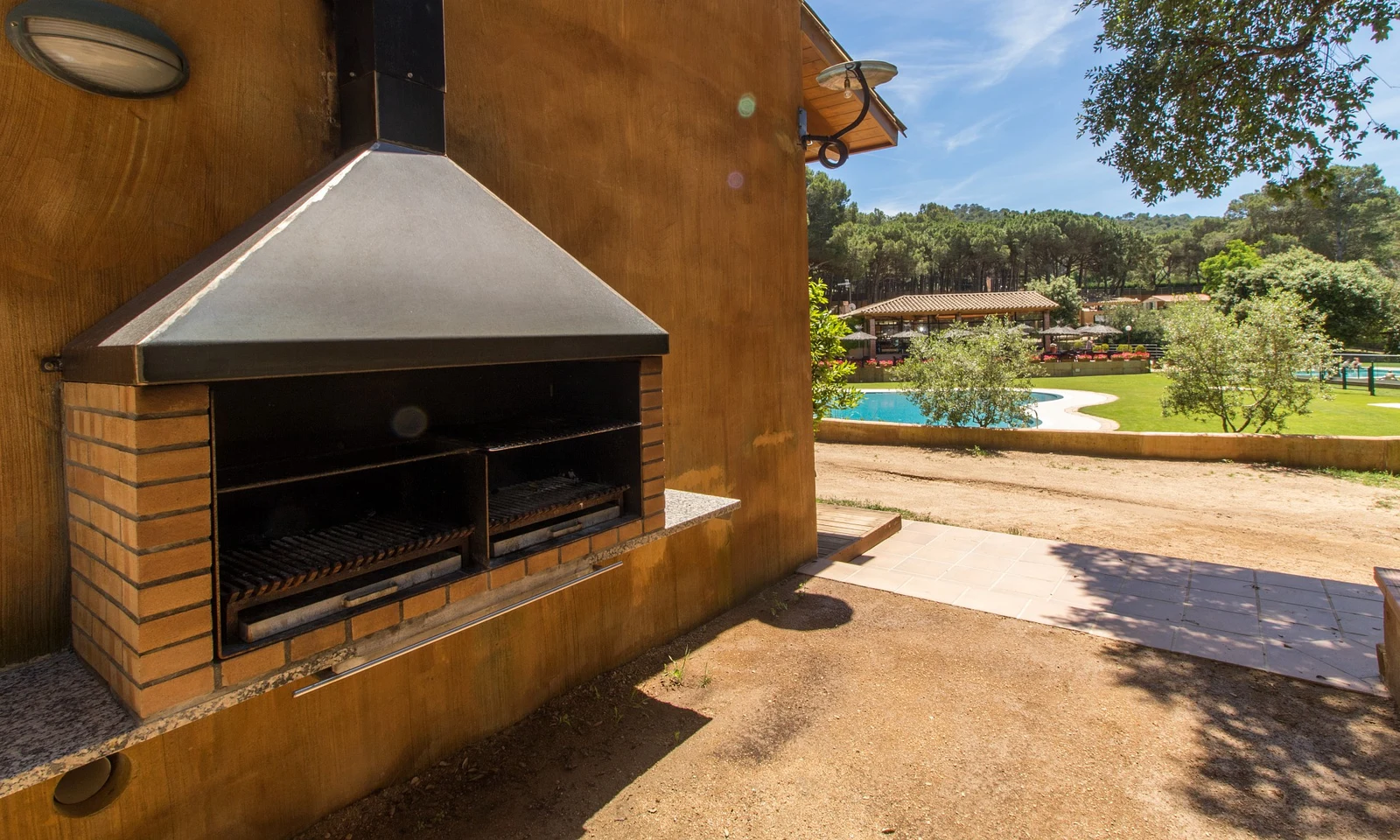 Brick barbecue station attached to a wall, overlooking a pool and lush green area, sunny day at Begur