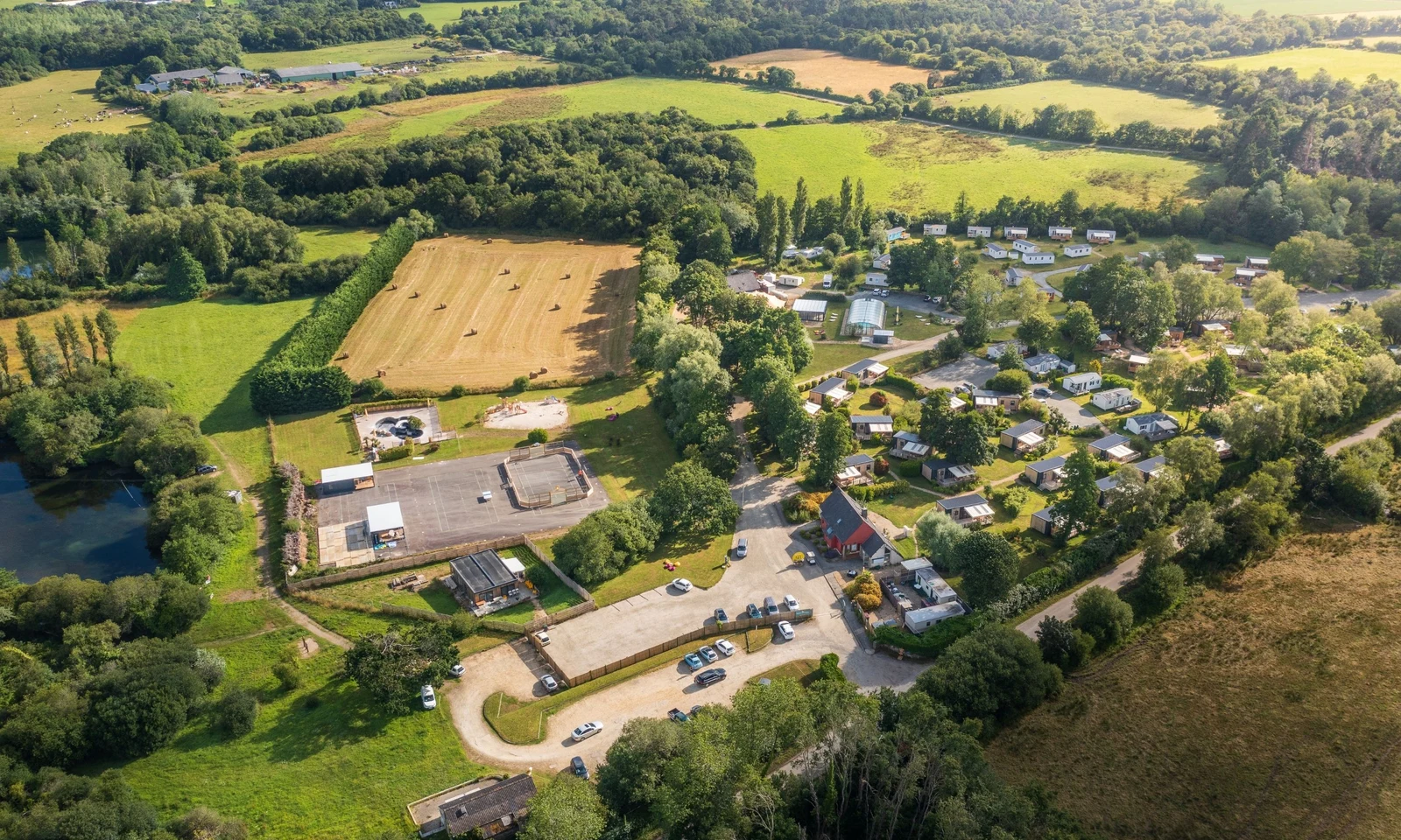 Aerial view of a campsite with parked cars and cabins surrounded by trees and fields at Domaine de Mesqueau