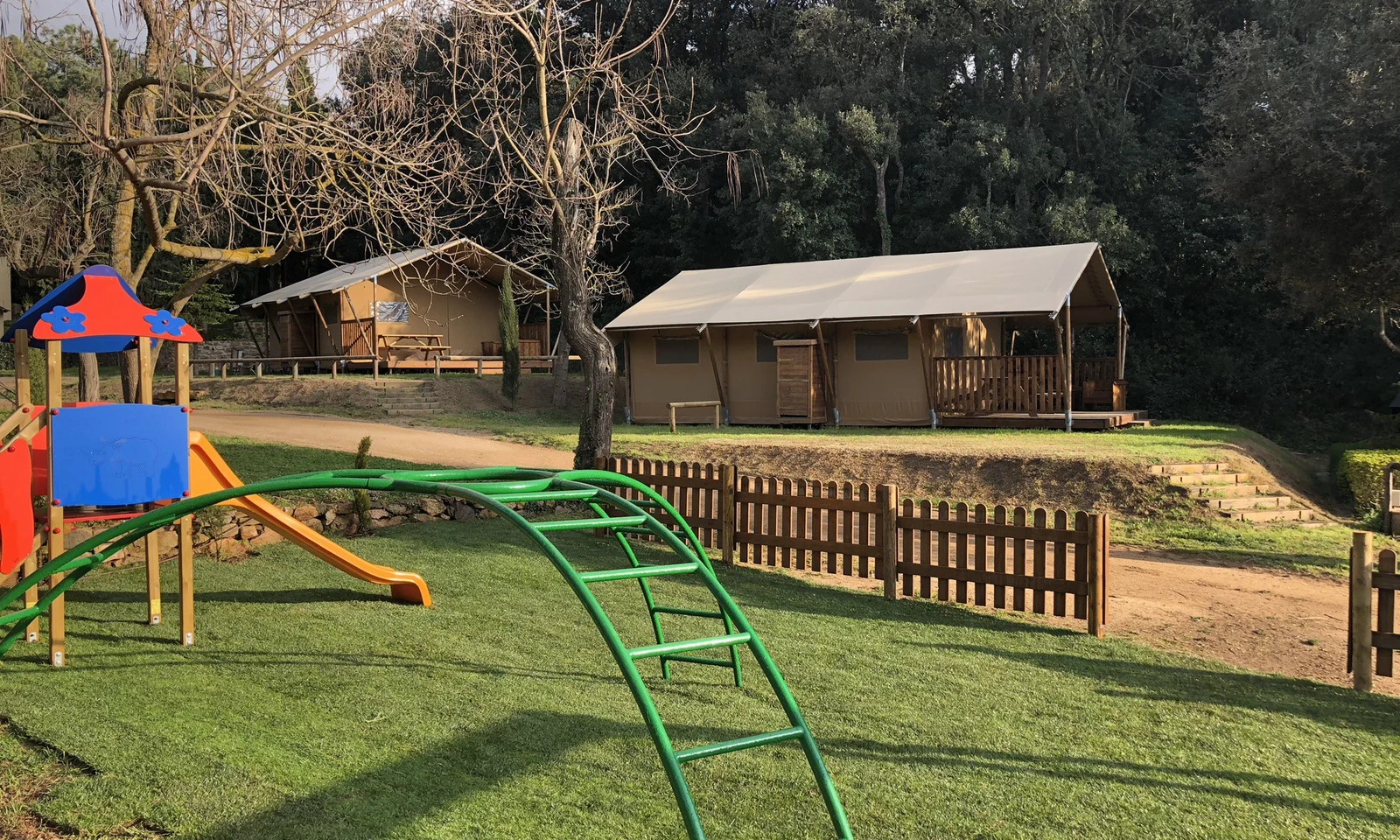 Playground featuring a slide and climbing frame, surrounded by wooden cabins and trees at Begur