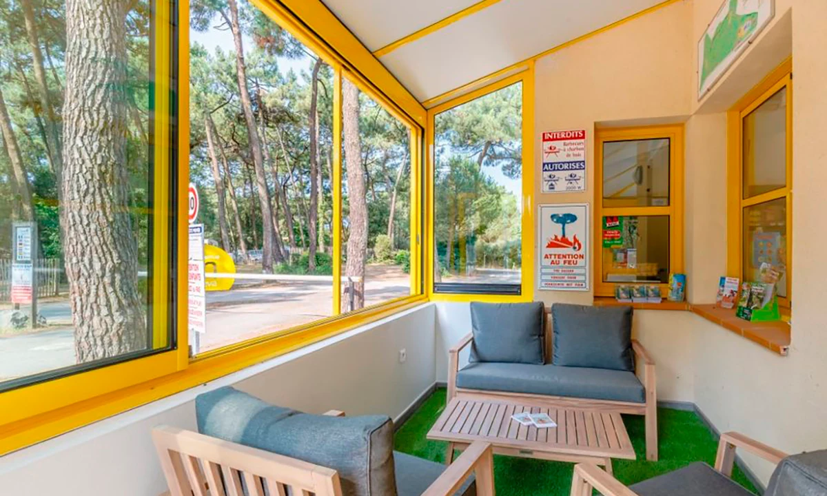 Wooden chairs with gray cushions arranged around a table in a sunlit room with large windows, overlooking a forest at Camping 2 Plages & Océan Village Corsaire