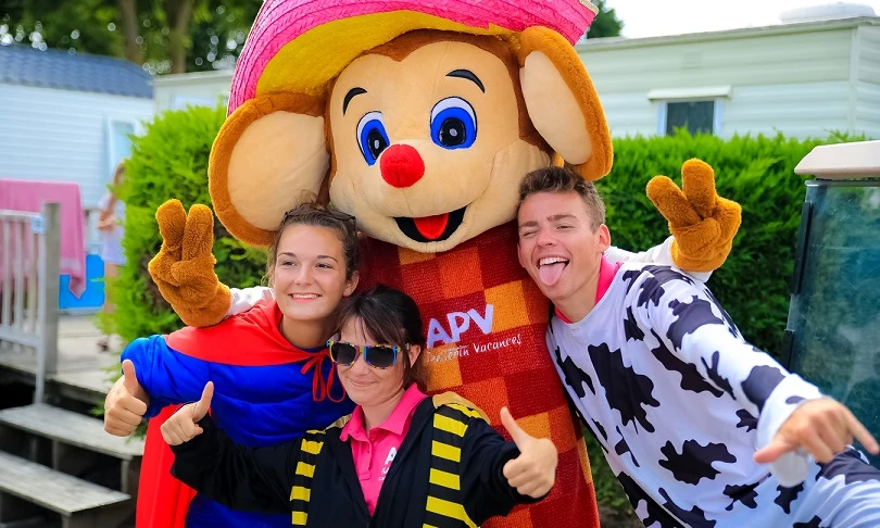 A costumed character poses with three smiling people outdoors near mobile homes and greenery at Les Aventuriers de la Calypso