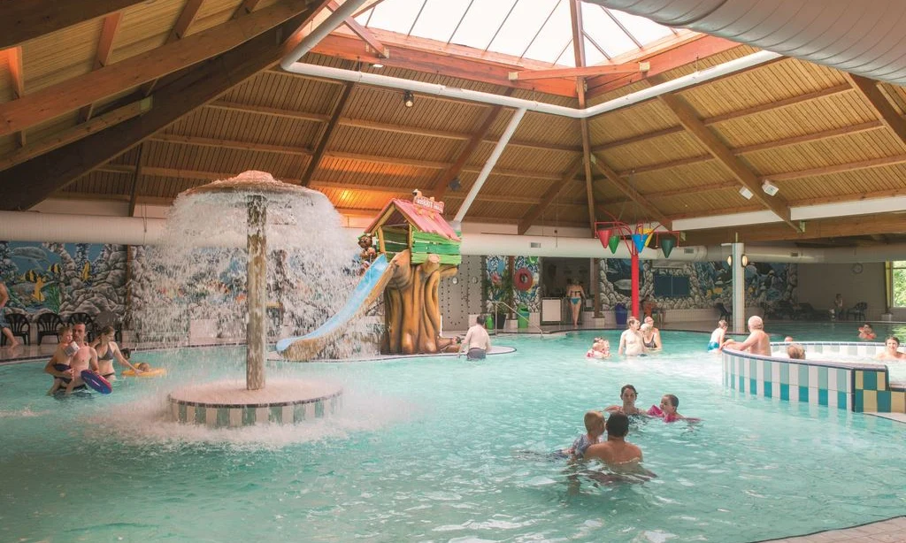 Indoor pool with people swimming and playing under a mushroom fountain and on a slide at Landal Rabbit Hill