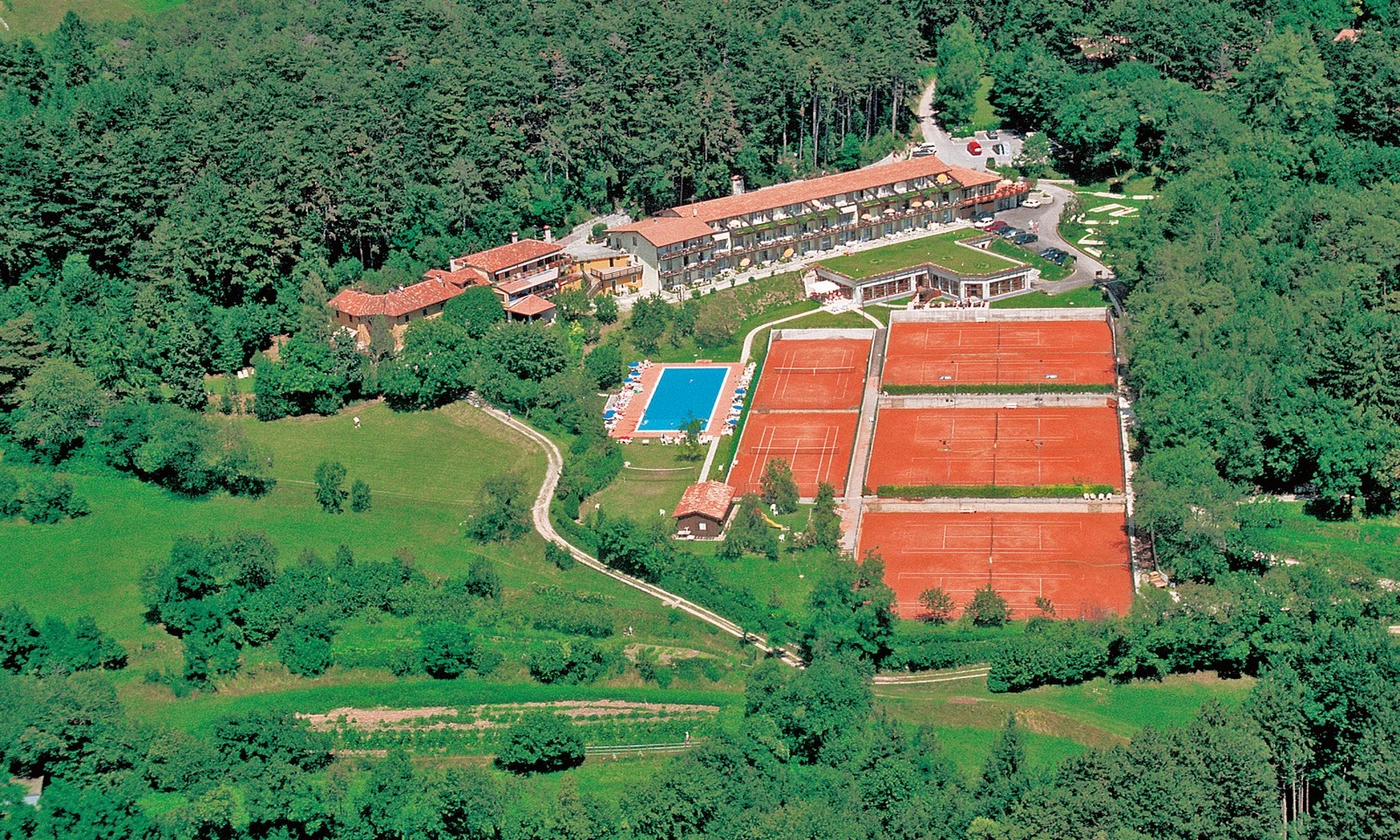 Aerial view of a resort amidst greenery, featuring multiple tennis courts, a swimming pool, and various buildings at Residence Campi