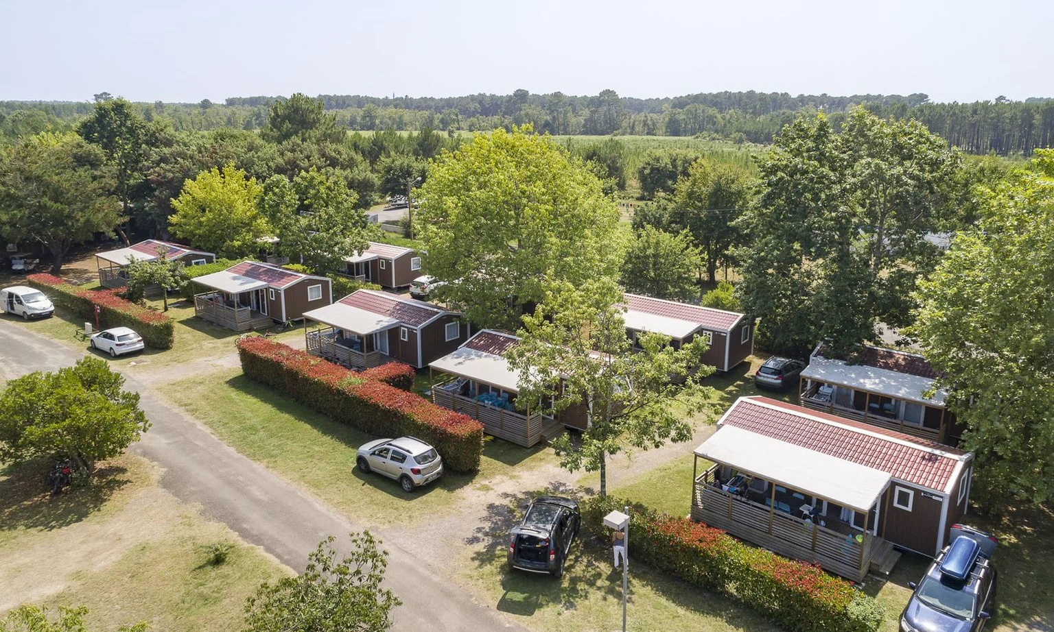 Rows of small cabins surrounded by trees and parked cars on a sunny day at Lac de Sanguinet