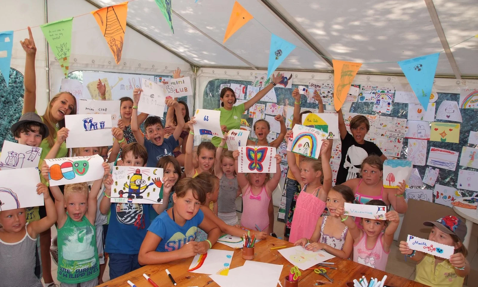 Children displaying drawings in a tent decorated with colorful bunting during an art activity at Leï Suves