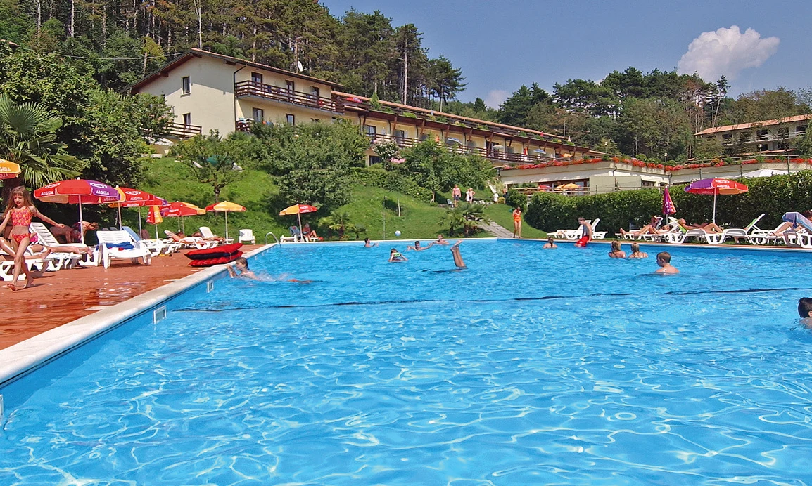 Pool with swimmers and sunbathers under umbrellas, surrounded by hillside villas and lush green trees at Residence Campi