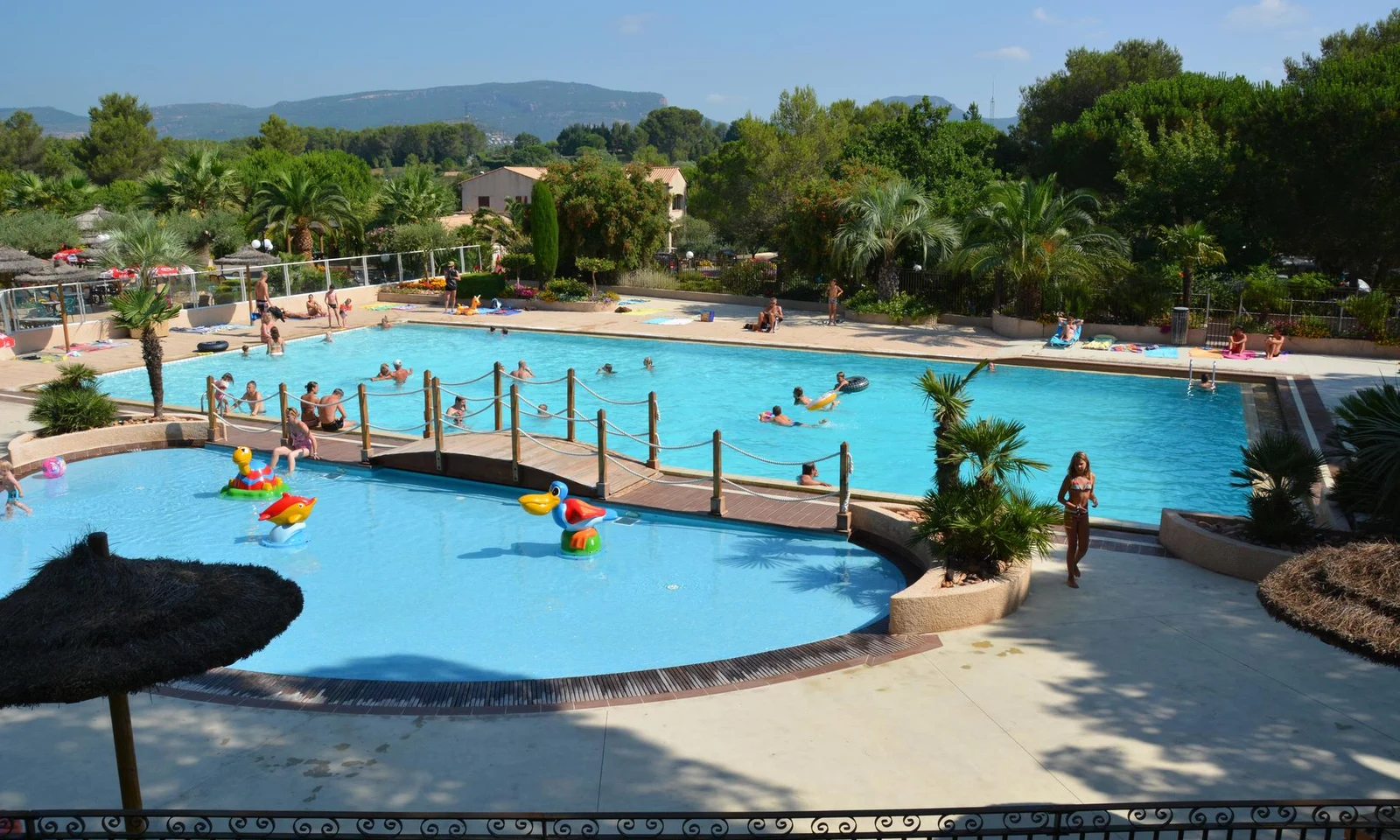 People swimming and relaxing in a large outdoor pool area surrounded by lush greenery and mountains at Leï Suves