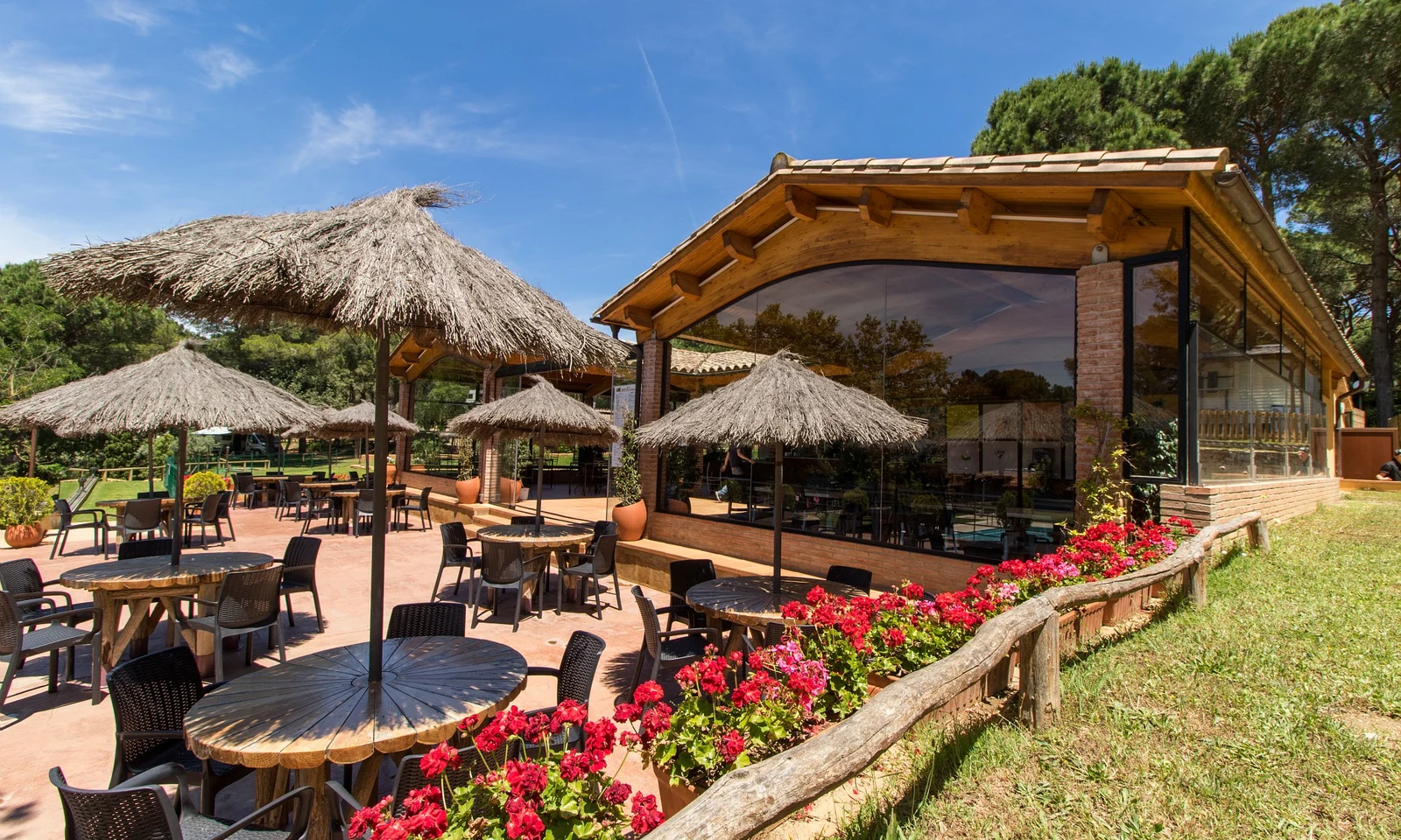 Outdoor dining area with wooden tables and thatched umbrellas, surrounded by vibrant flowers and greenery at Begur