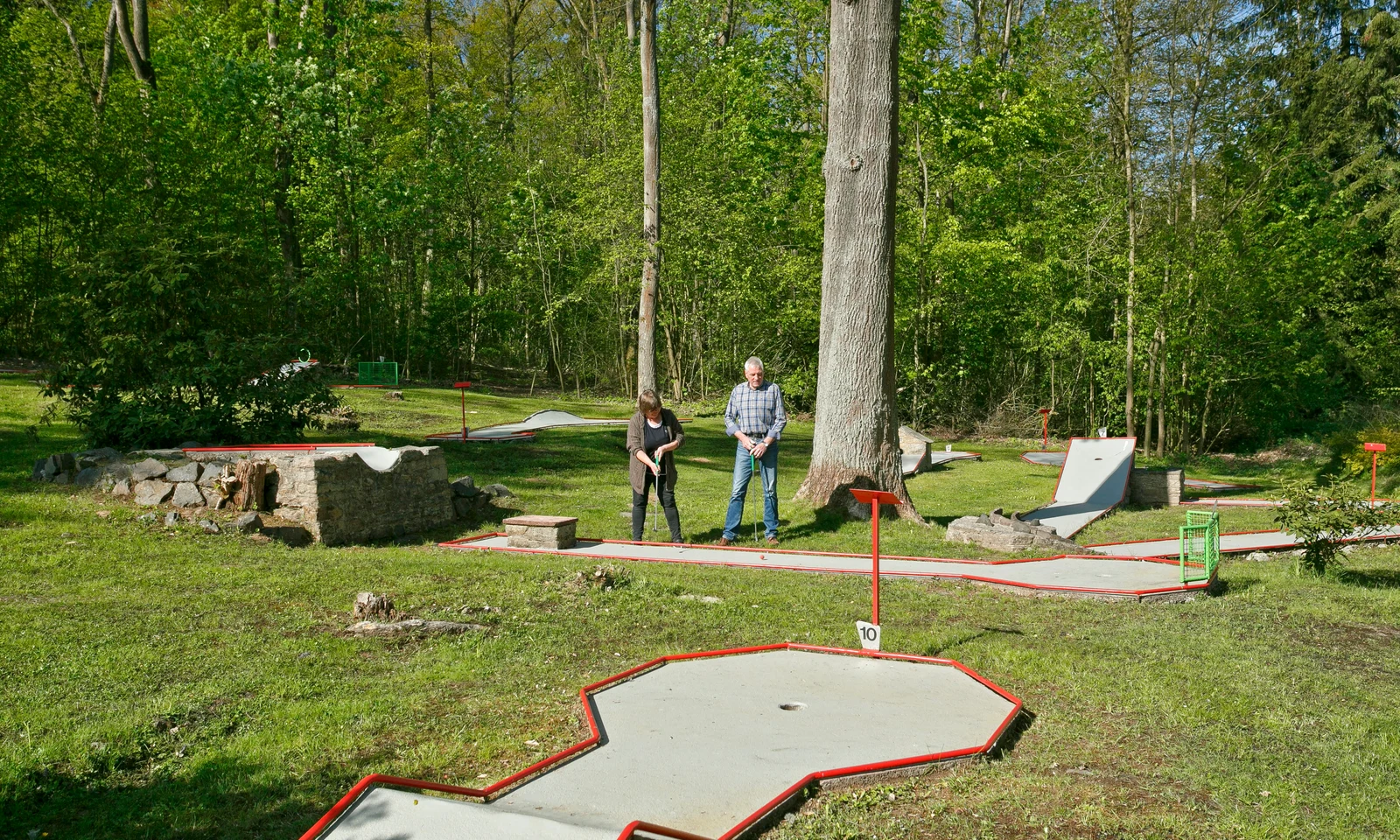 Two individuals playing mini-golf surrounded by trees and greenery at KNAUS Campingpark Hünfeld