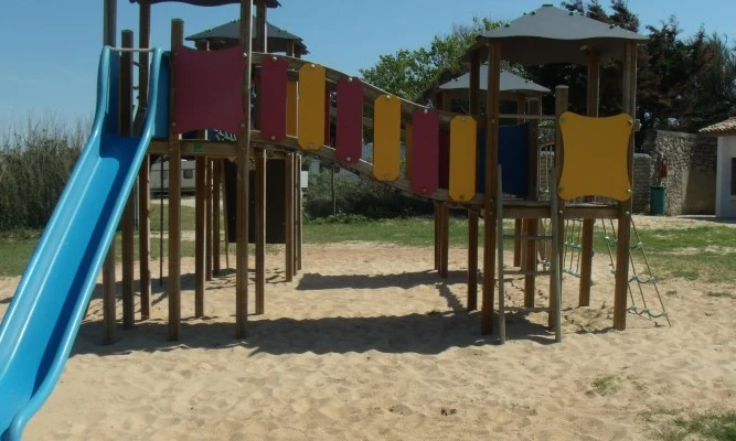 Playground structure with slide and bridge on sand surrounded by grassy area and barbecue station at Seasonova Ile de Ré