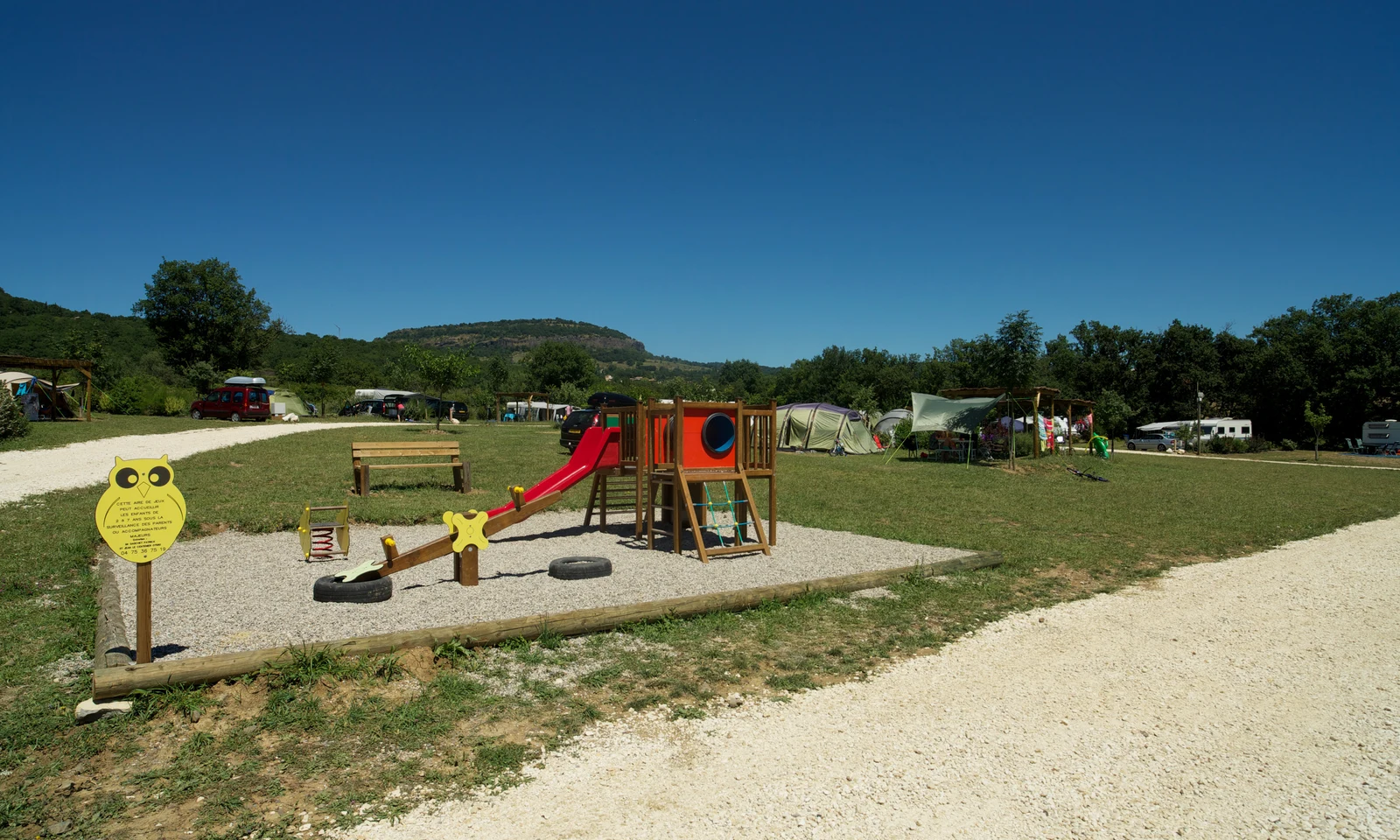 Playground with slide and seesaw, surrounded by tents and greenery under a clear blue sky at Les Arches