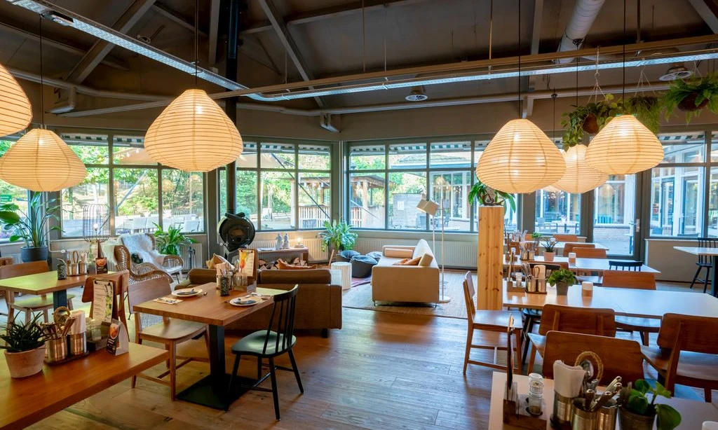 Dining tables with place settings surrounded by chairs and sofas, with hanging lanterns illuminating a cozy, modern interior at Landal Rabbit Hill