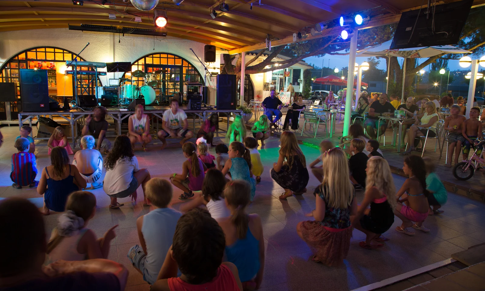 Children dancing in front of an outdoor stage during a festive evening, with people seated and watching at Bon Repos