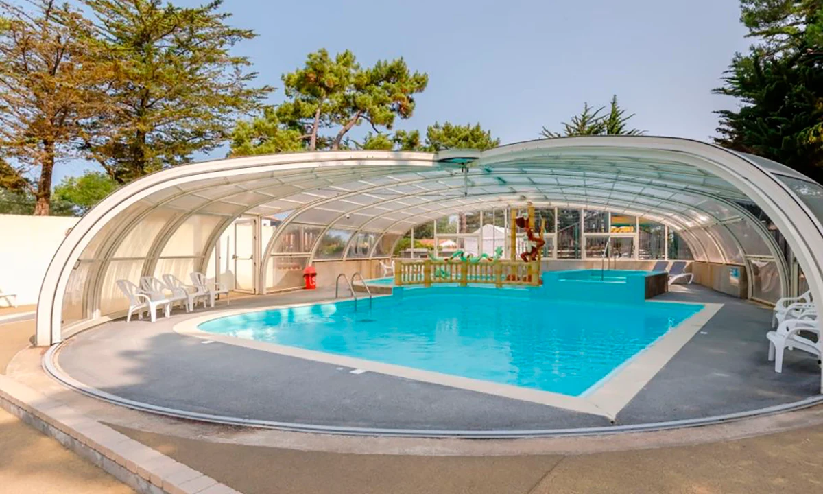 Covered swimming pool with lounge chairs, surrounded by trees in an outdoor campsite setting at Camping 2 Plages & Océan Village Corsaire