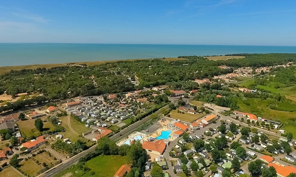 Aerial view of a coastal campsite with numerous RVs, a swimming pool, and surrounding lush greenery at Les Aventuriers de la Calypso