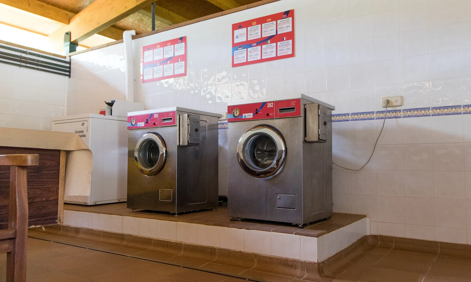 Two washing machines on a tiled platform in a clean laundry room with wooden ceiling beams at Begur